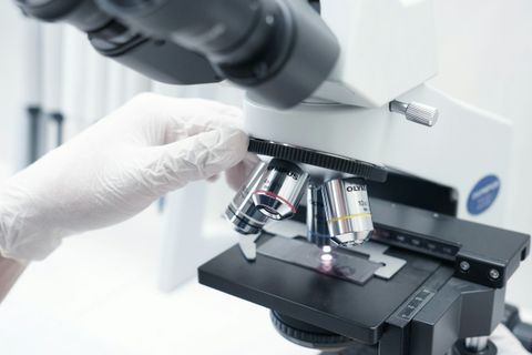 Hand met handschoen die de objectieven van een labomicroscoop draait